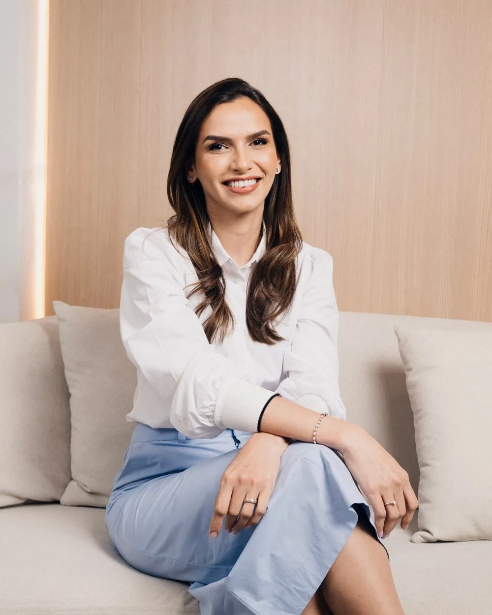 Dra. Anne Caroline Amorim, ginecologista, sorrindo sentada em um sofá claro